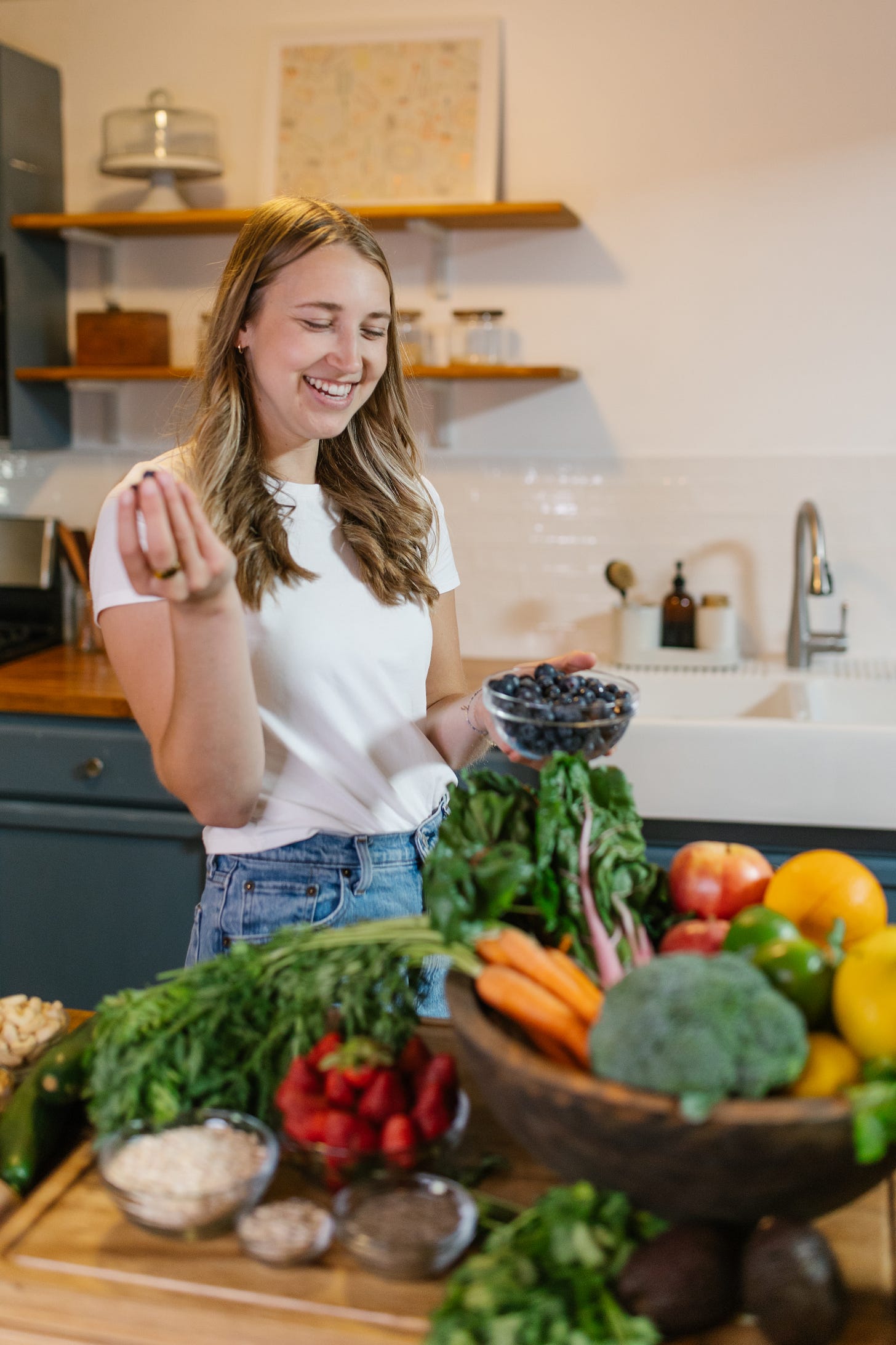 girl in the kitchen with many nourishing foods and vegetables to support hormone health and feel more energized and balanced throughout the month 