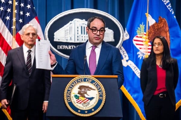 Jonathan Kanter holds up documents while standing behind a lectern with the Justice Department’s seal on it. 