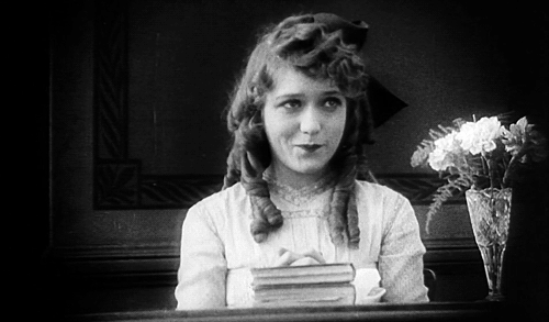An animated GIF of silent movie actor Mary Pickford covering her mouth as she giggles in the 1917 film The Poor Little Rich Girl