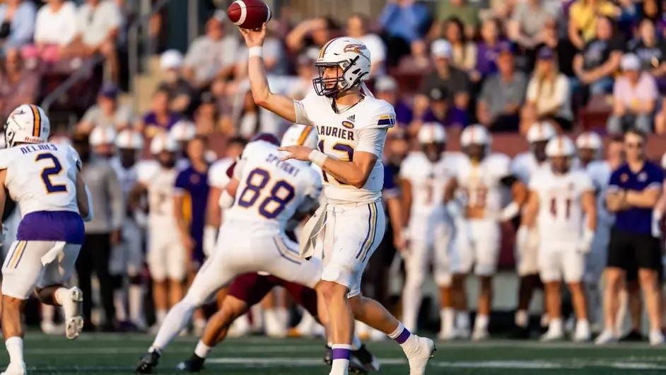 Football player in white uniform throwing a ball as his teammates block for him.