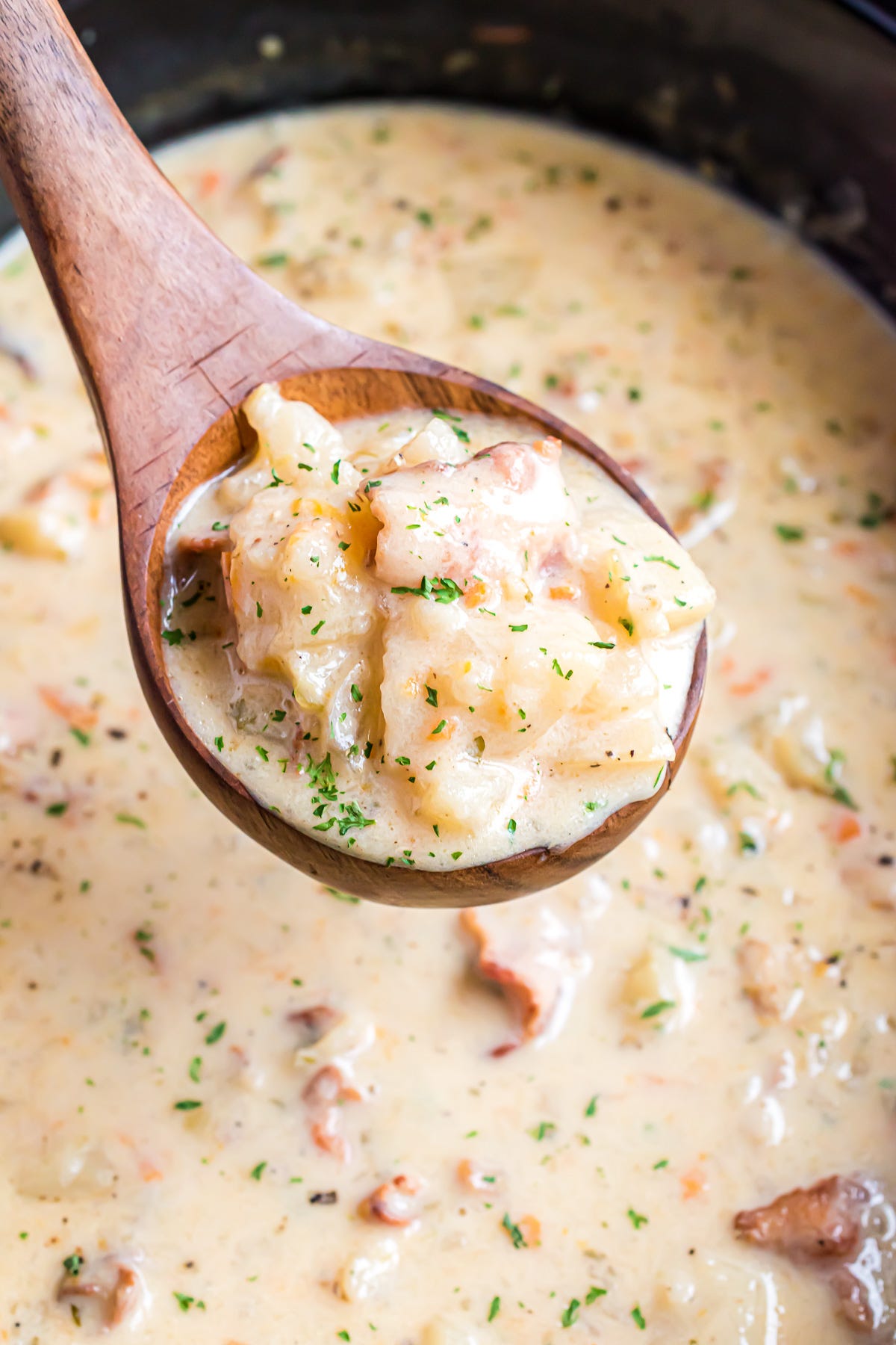 A wooden ladle hovering above a slow cooker filled with creamy potato soup.