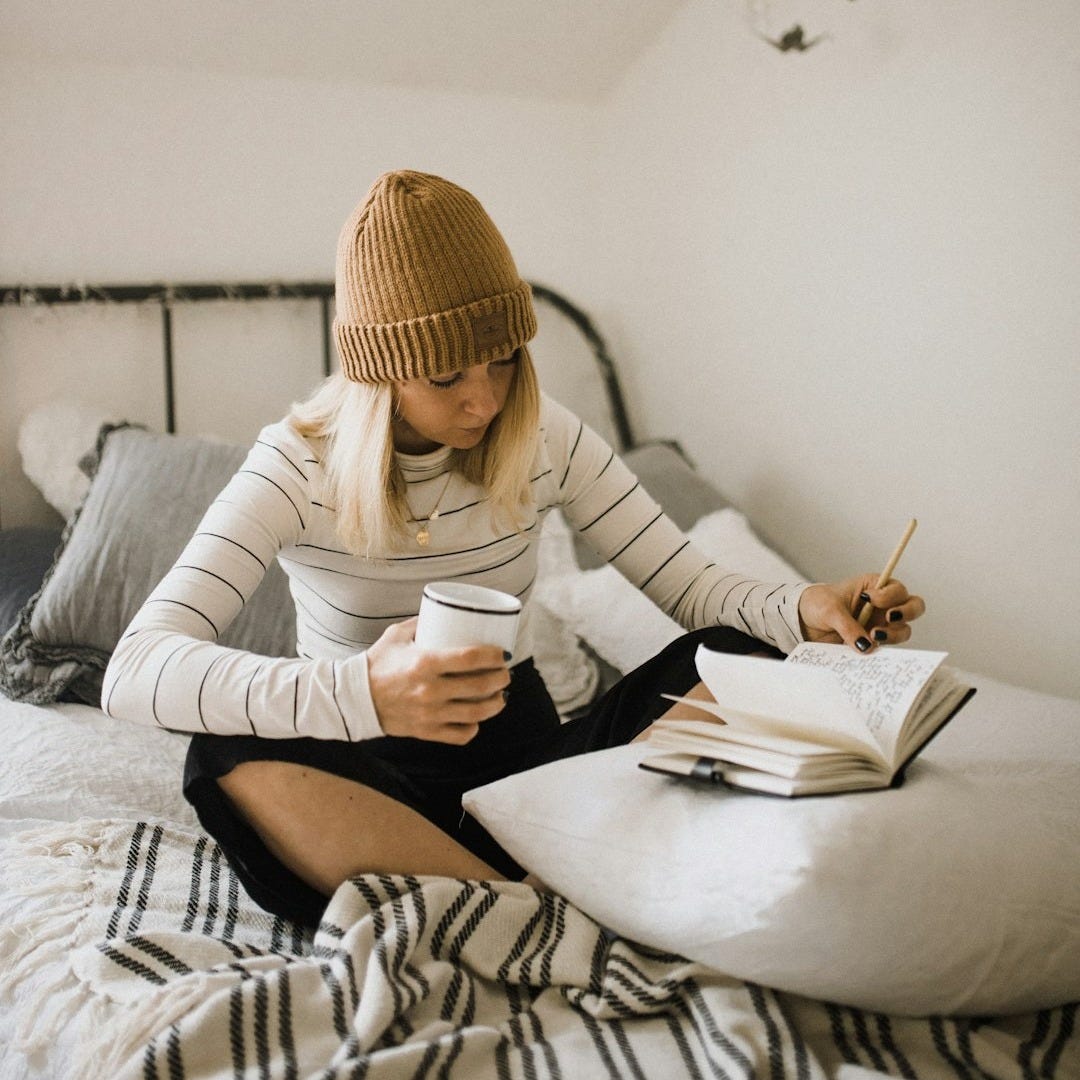 woman in striped shirt sitting on bed while writing woman in striped shirt sitting on bed while writing