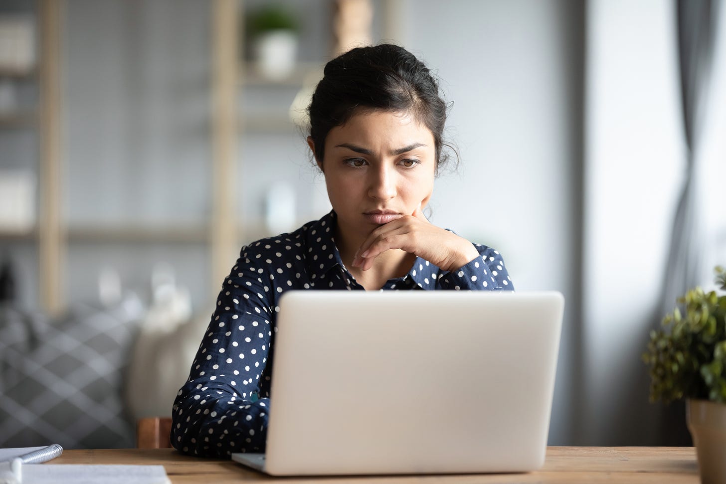 A young woman frowns at her laptop screen