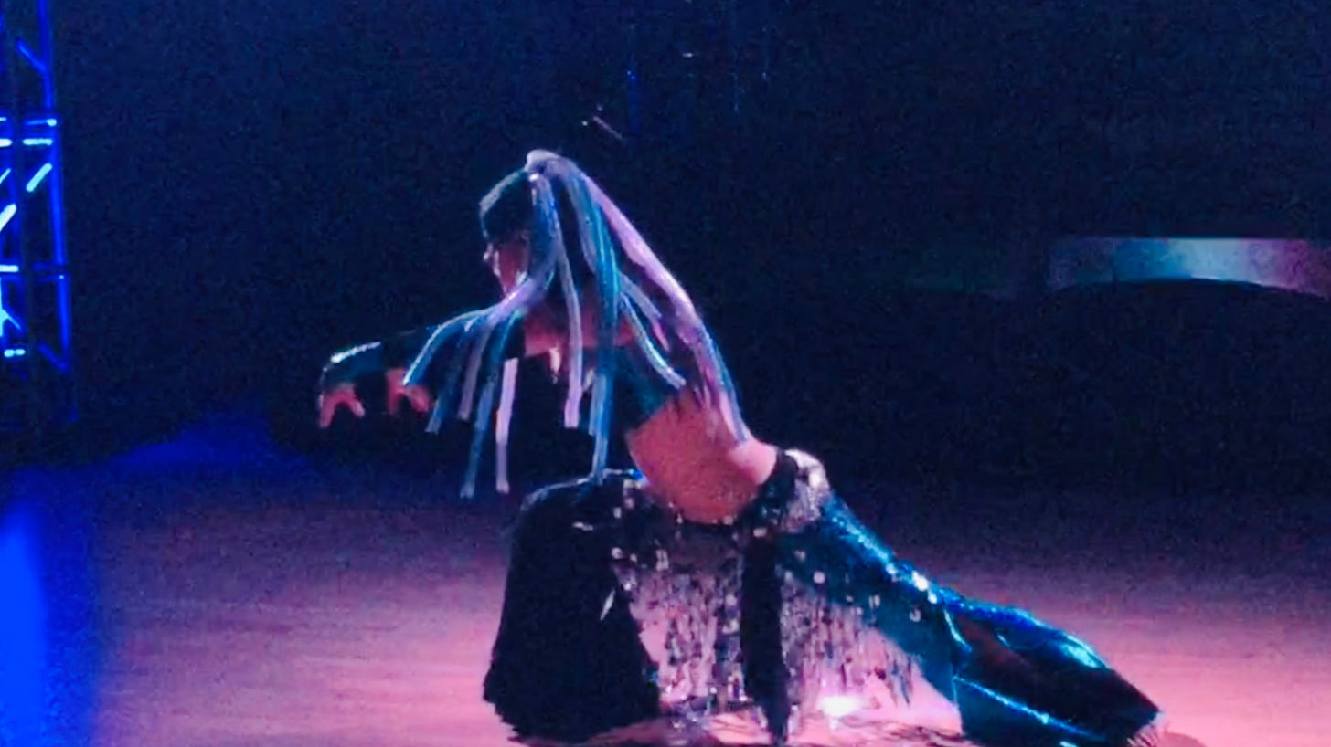 The author wafting ocean-arms in black and turquoise mermaid pants, a silver net hip scarf, and a headdress of turquoise and opalescent springy filaments