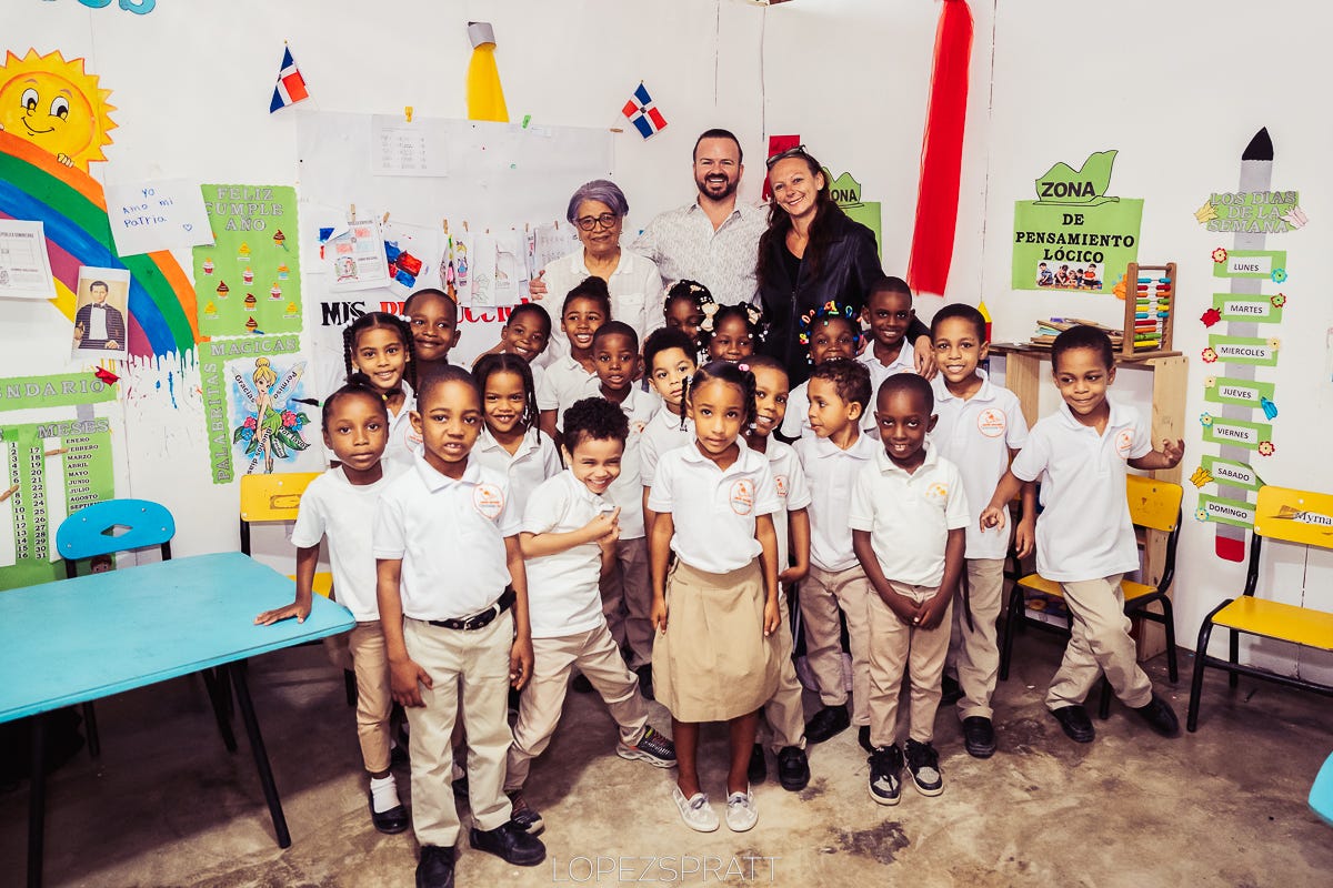 Photo of a dozen students standing inside one of our classrooms, with colorful student projects and Dominican flags on the wall.