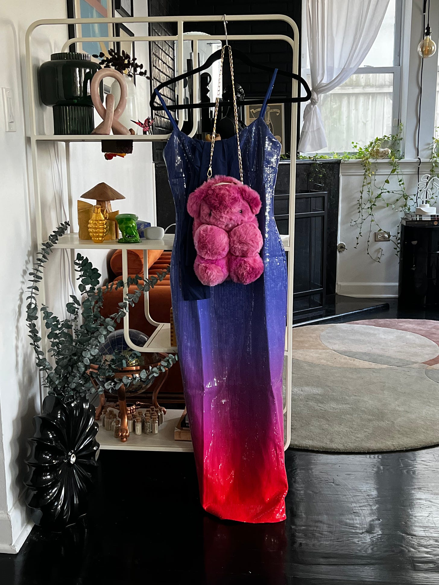 Long ball gown dress featuring a blue to pink gradient with pink teddy bear bag hanging in a living room.