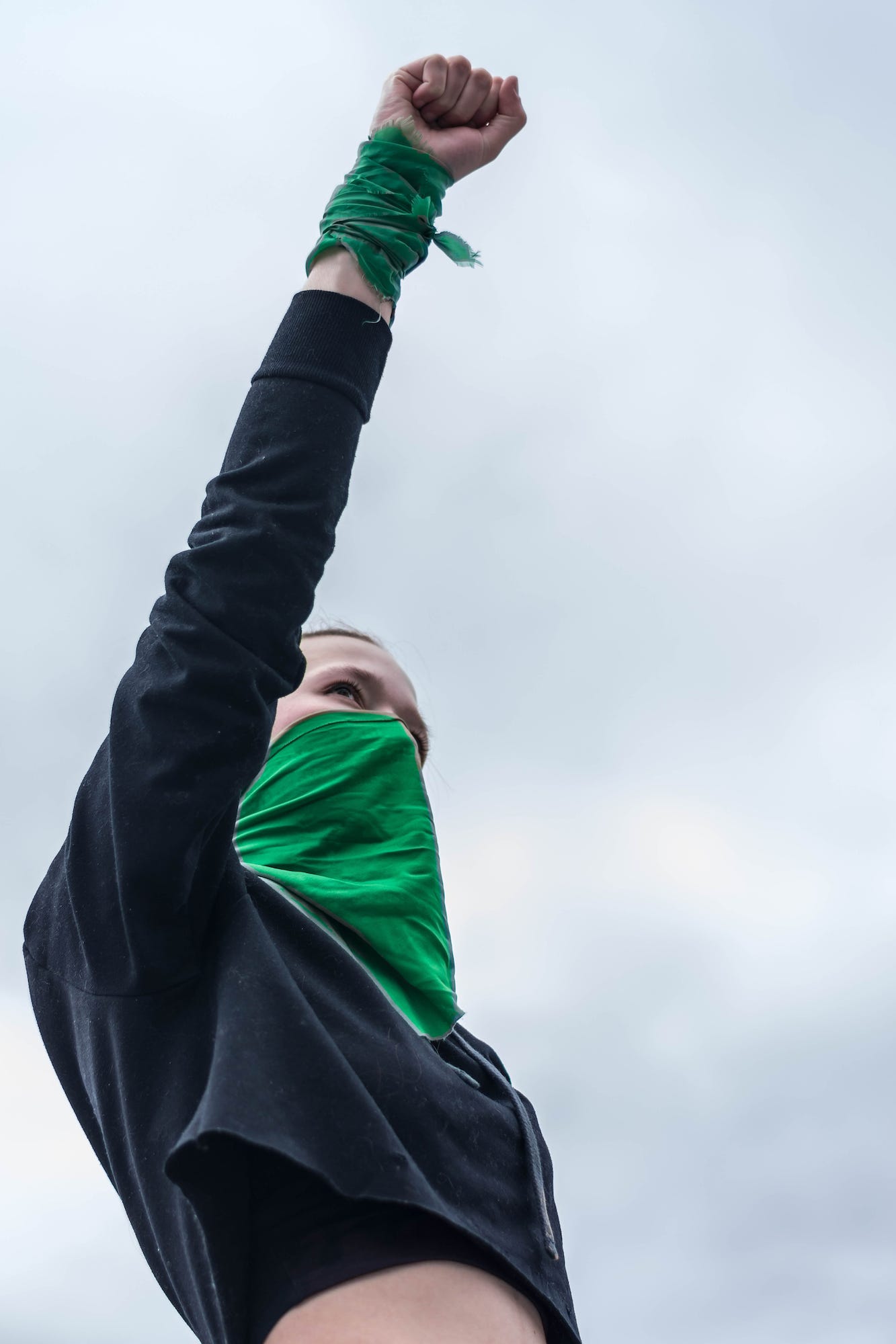 Woman wearing green bandana across face standing with fist raised