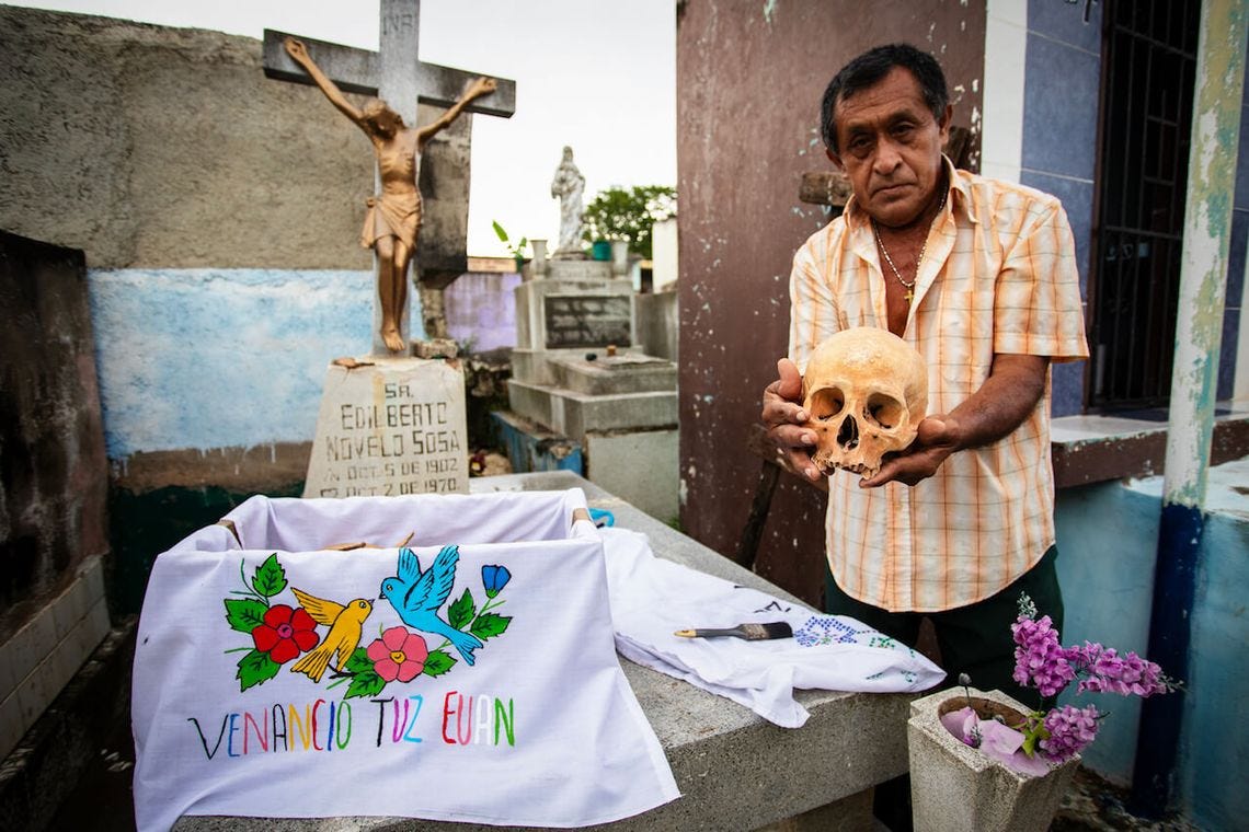 Don Venancio drží lebku a vysvětluje dušičkovou tradici v mexickém pomuchu na yucatánu, při které se vyjímají ostatky mrtvých z hrobů a vystavují se. 