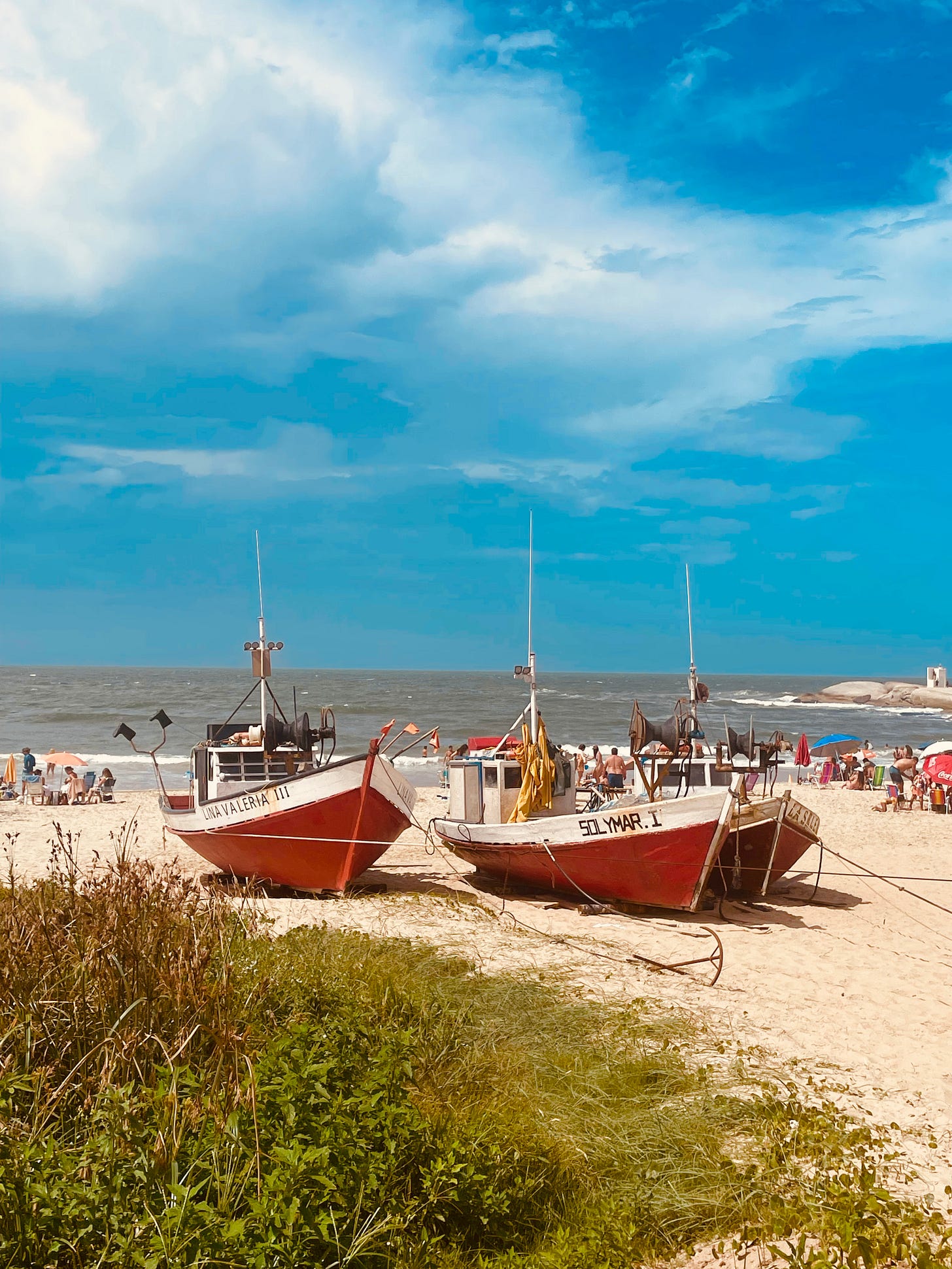 red and white wooden fishing boats sitting on the beach on a sunny day with blue sky