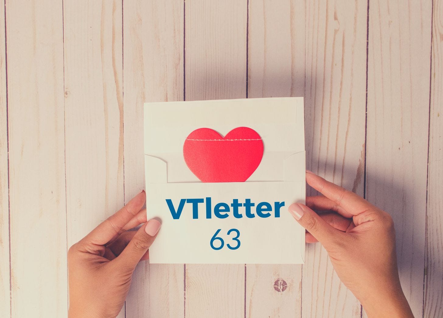 Mãos femininas sobre mesa de madeira segurando envelope aberto com carta contendo um coração e nome VTletter 63.