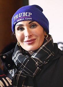 Headshot of Laura Loomer speaking at an event, wearing a MAGA beanie.