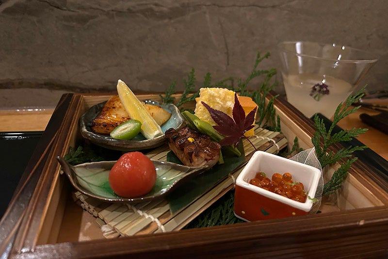 A plate full of fish, salmon row, vegetables and framed by pine leaves.