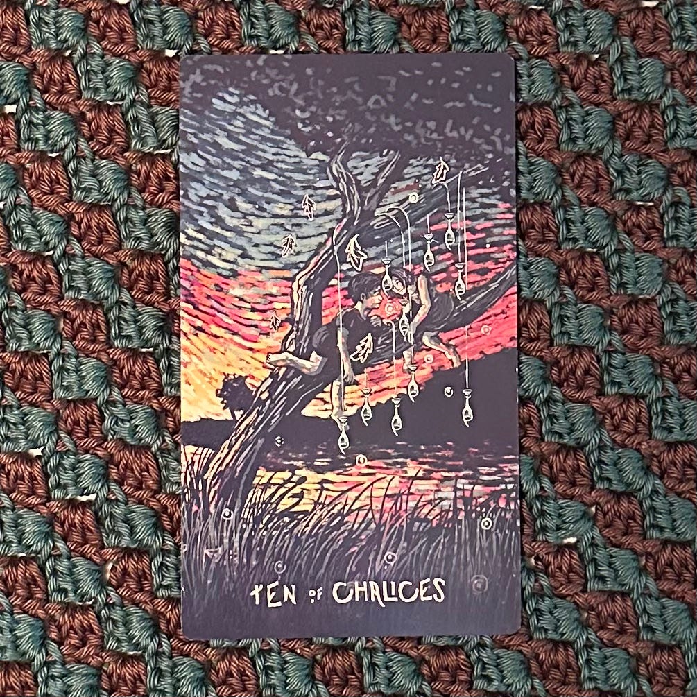 Ten Chalices dangle from the branches of a tree, each looped with its twin in perfect, staggered balance. Two children sit in the crook of the tree, gazing at each other with gratitude and love. The river flows calmly, its soft, rustling presence lilting gently beneath.