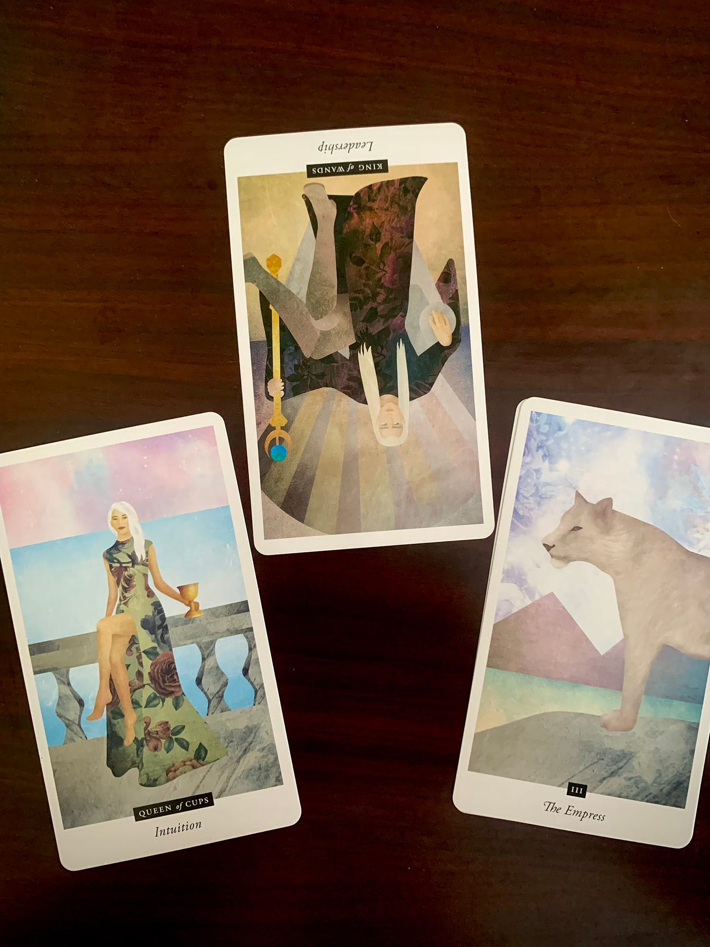 Three tarot cards on a brown table. The Queen and King of Wands and the Empress.