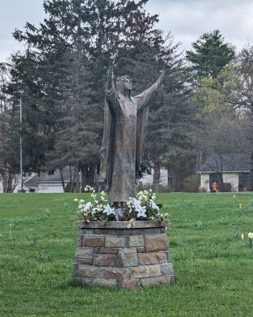 statue with arms outstretched and flowers at her feet