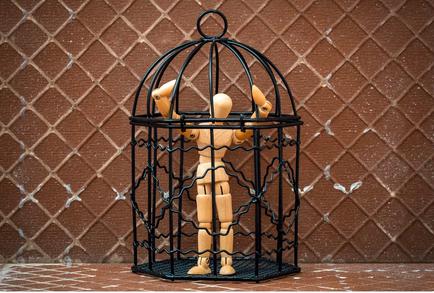 Artist dummy trapped in black bird cage brown background