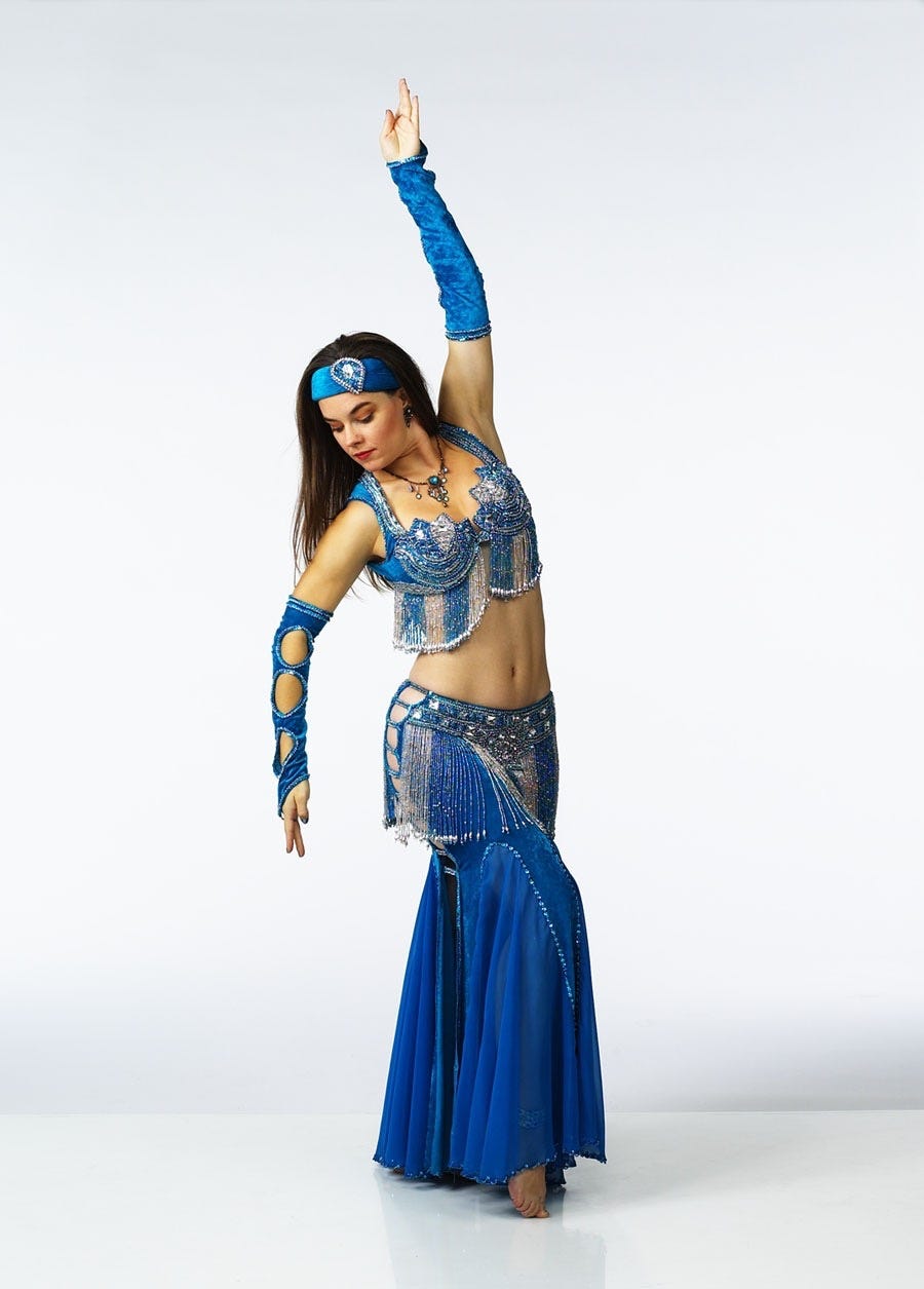 The author posed in a turquoise-and-silver belly dance costume, draped in beaded fringe with cut-outs along the hips and the opera-length gloves.