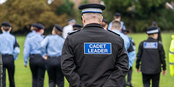 Volunteer police cadet leader walks behind uniformed police cadets 