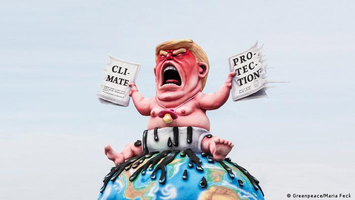 Trump sitzt mit Schnuller um den Hals auf einem Globus. In jeder Hand einen Teil des zerissenen Klimaabkommens. Schloss Oberhausen Ludwiggalerie Ausstellung Jacques Tilly (Greenpeace/Maria Feck )