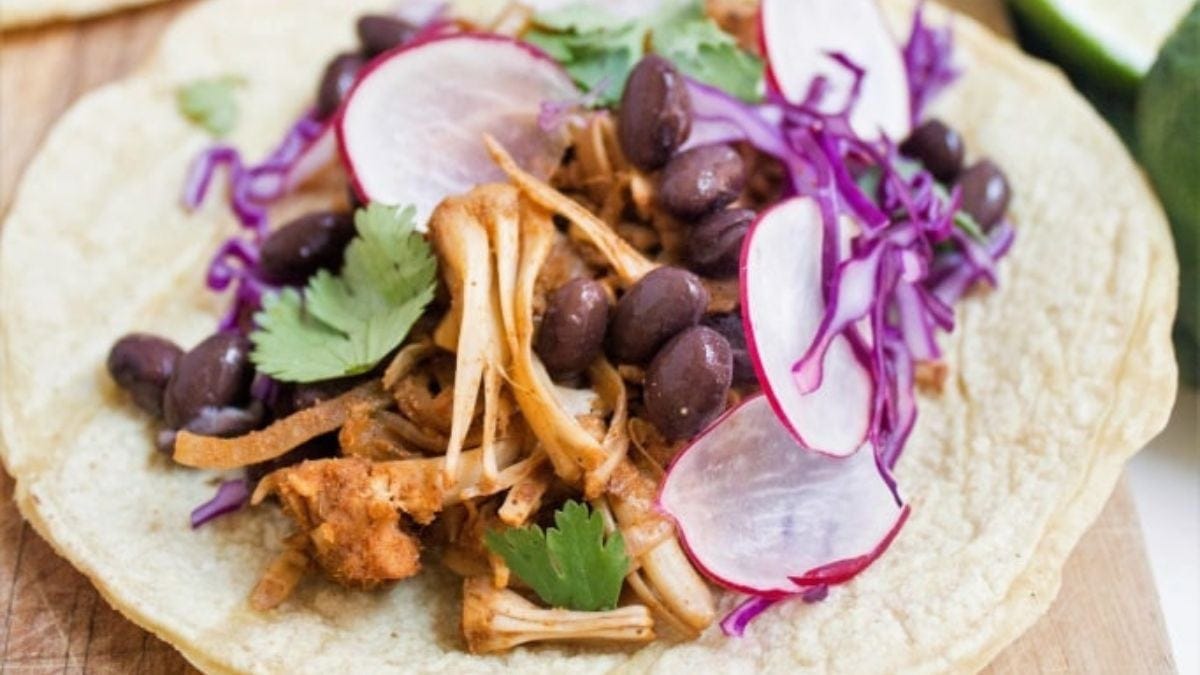 A vibrant taco filled with shredded chicken, black beans, sliced radishes, red cabbage, and fresh cilantro on a soft tortilla, displayed on a wooden surface.
