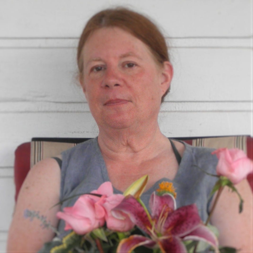 Leslie Golding Mastroianni is a white skinned woman with light brown hair pulled back from her face. She poses with a vase of pink flowers.