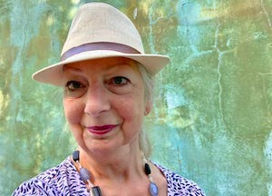 image of mature white woman wearing a hat. Yasmin Chopin is host of Place Writing community and publication.