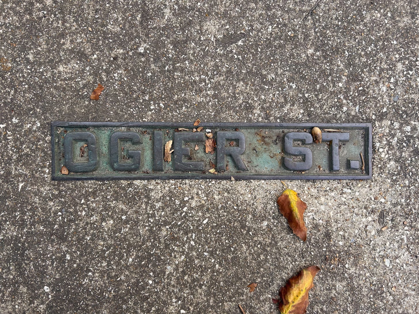 Metal Ogier street sign in sidewalk and two autumnal golden leaves