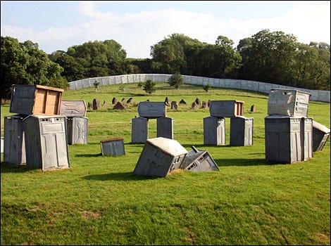 A photo of a grassy knoll on a sunny day with portable toilets stacked up in a circle formation resembling Stonehenge