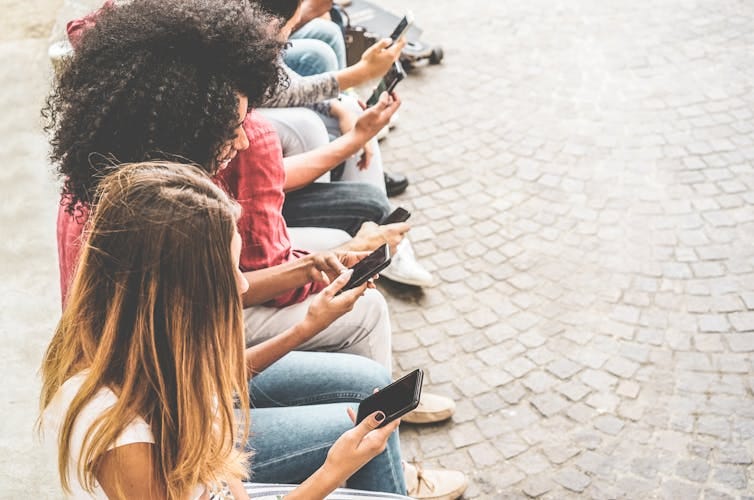 An overhead shot of women sitting in a row and looking at their phones. An overhead shot of women sitting in a row and looking at their phones.