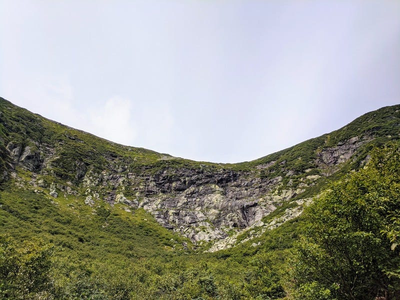 Tuckerman's Ravine at Mt Washington, a vast rounded bowl in the rock partially covered by green plants
