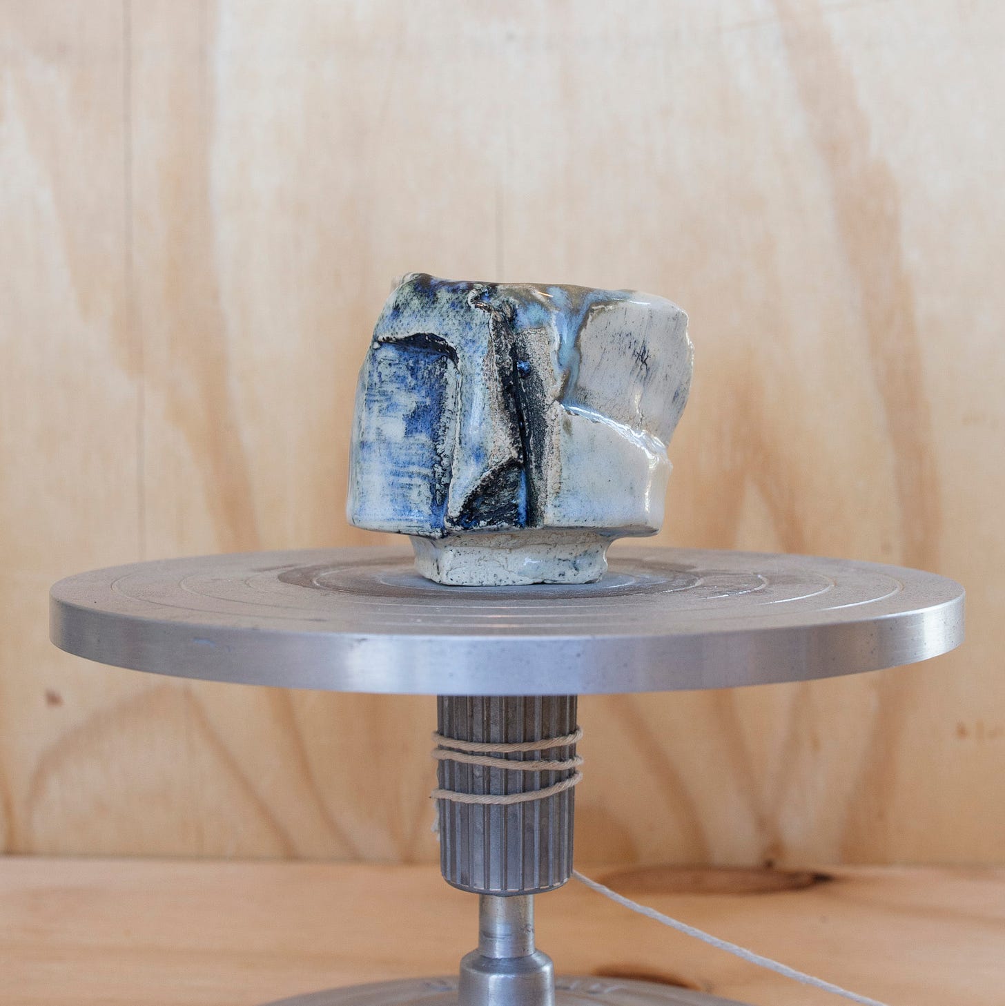 A carved clay cup in front of plywood and sitting on an aluminum stand.