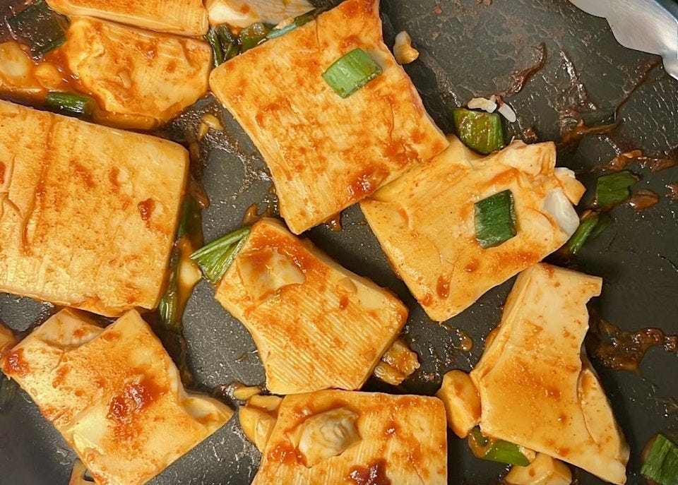 Gochujang-glazed tofu with scallions in a black skillet