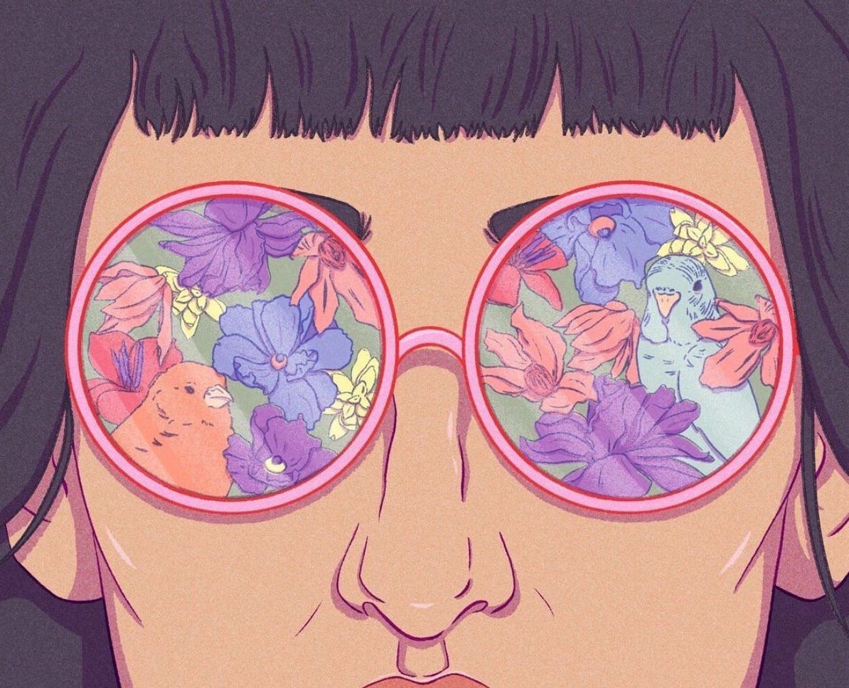 Extreme close-up of a face, cropped just above a straight fringe and below the nose, wearing large round pink glasses, which reflect a vibrant scene of birds and blossoming flowers.