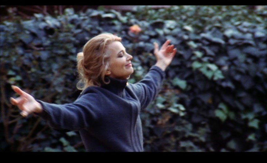 Gena Rowlands stands with her arms outstretched in front of a hedge, her eyes closed, in "A Woman Under the Influence" (1974)