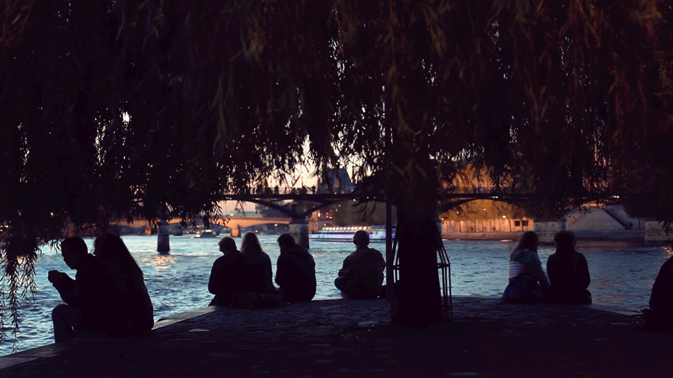 Photo prise depuis le bout du Square du Vert Galant, sur l'Île de la Cité, avec les silhouettes des gens qui se découpent sur la Seine.