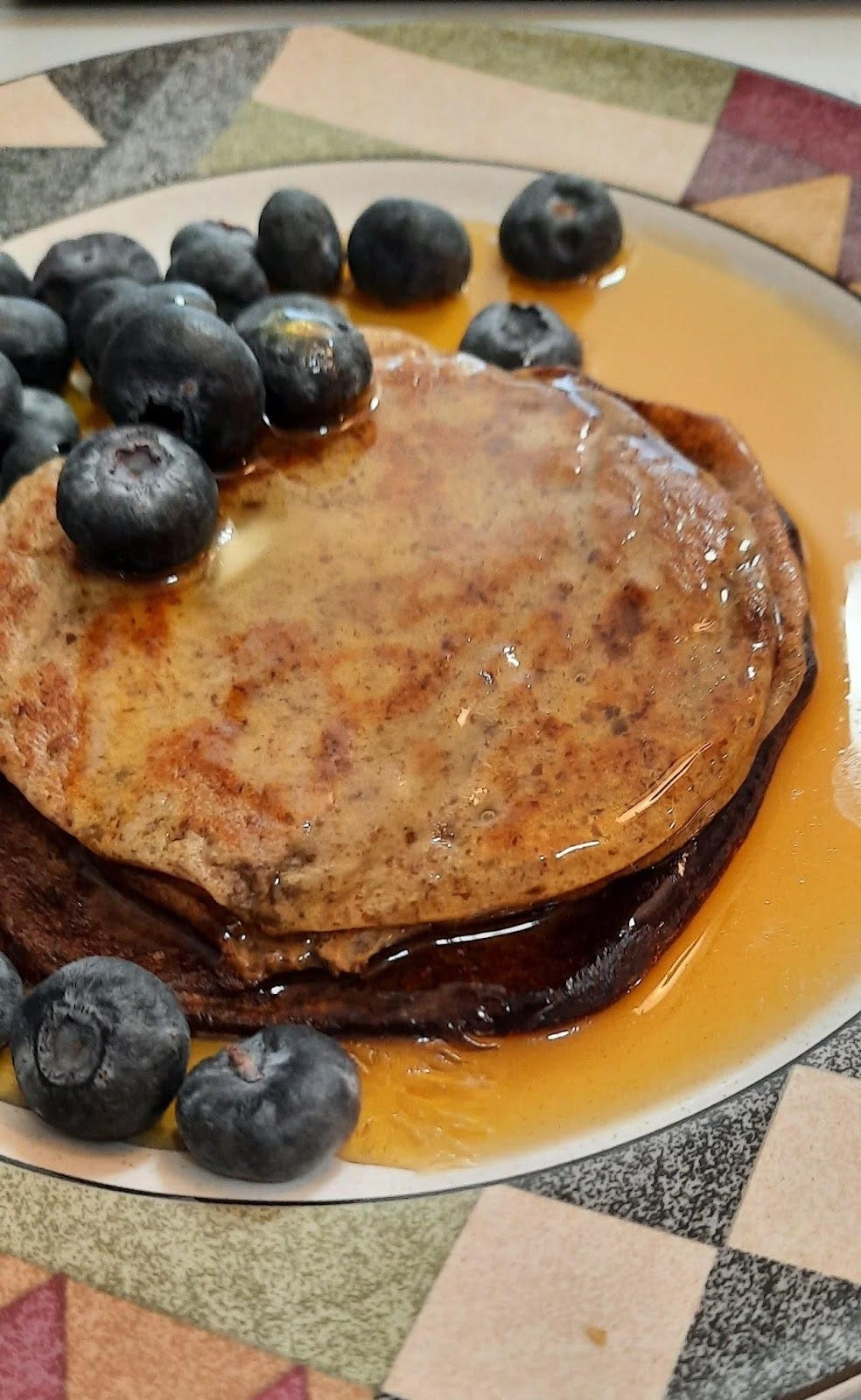 Pancakes, blueberries and too much maple syrup on a white plate with a colorful rim.