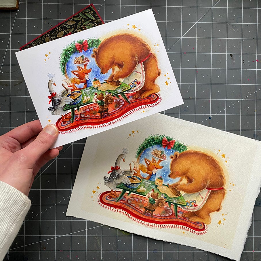 A printed christmas card featuring woodland animals baking cookies together, next to the original watercolor illustration.