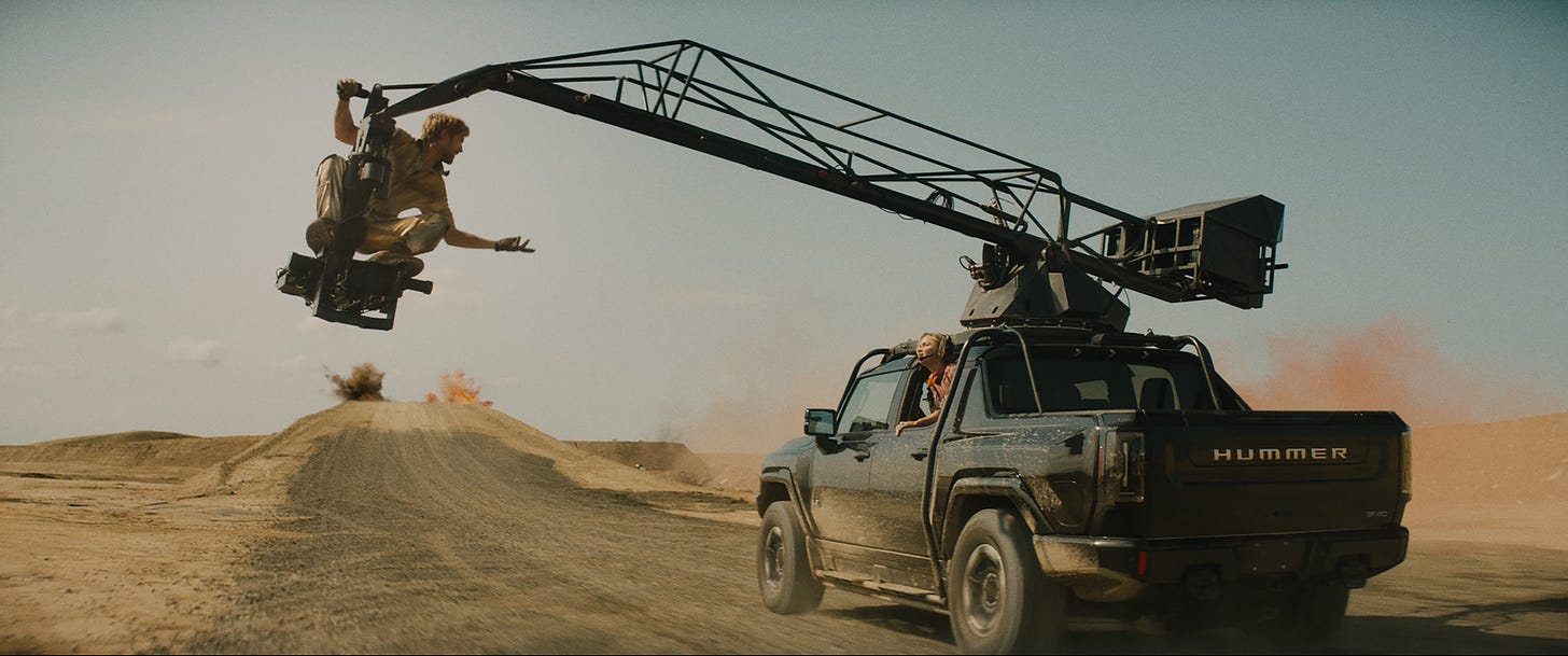 Ryan Gosling and Emily Blunt have a shouted conversation in The Fall Guy. He's a stunt man perched on a camera crane attached to a large car speeding down a dirt road, and she's looking back at him from one of the car's windows.