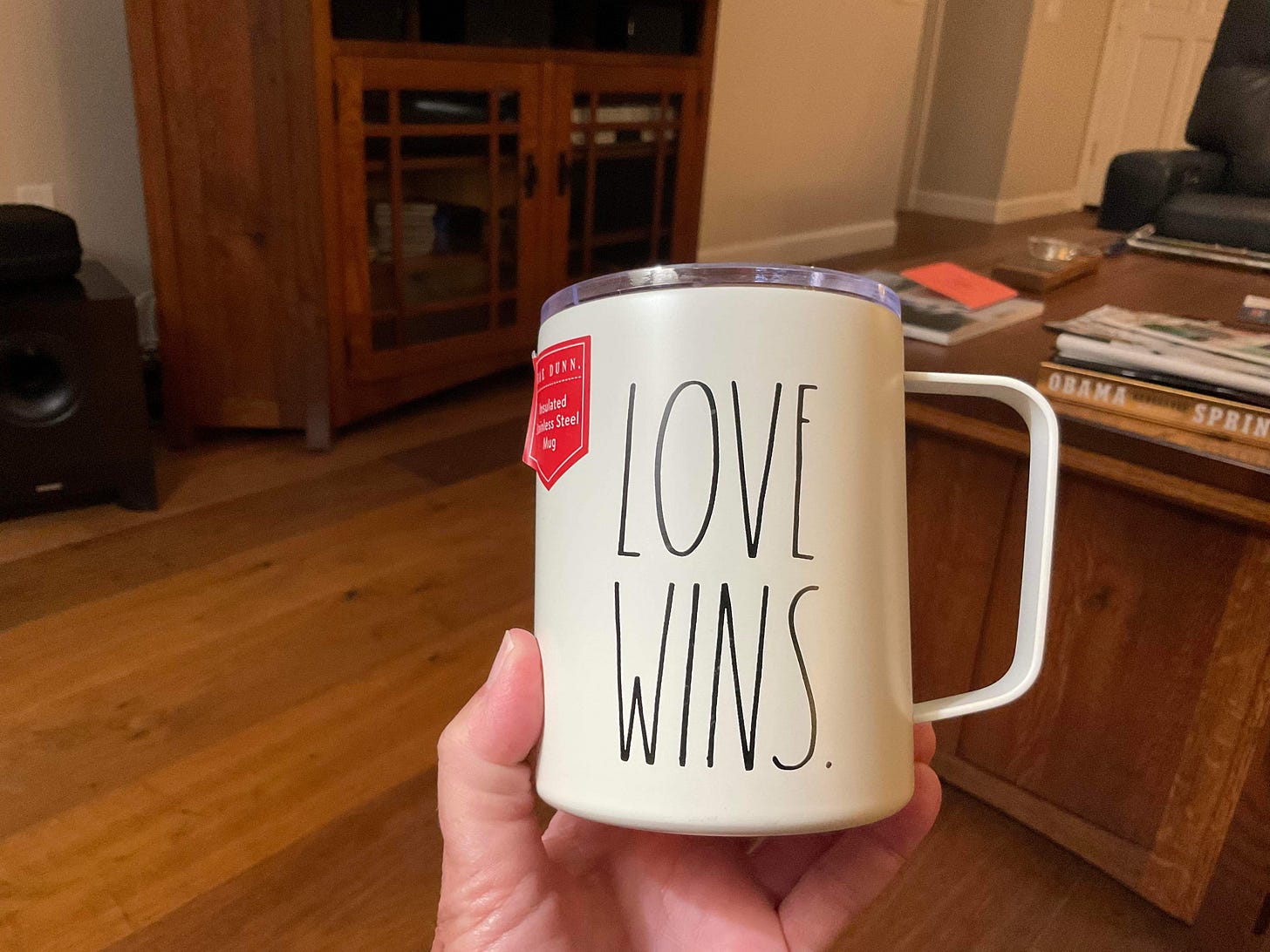 A white stainless steel coffee mug with the words “love Wins” printed on it.