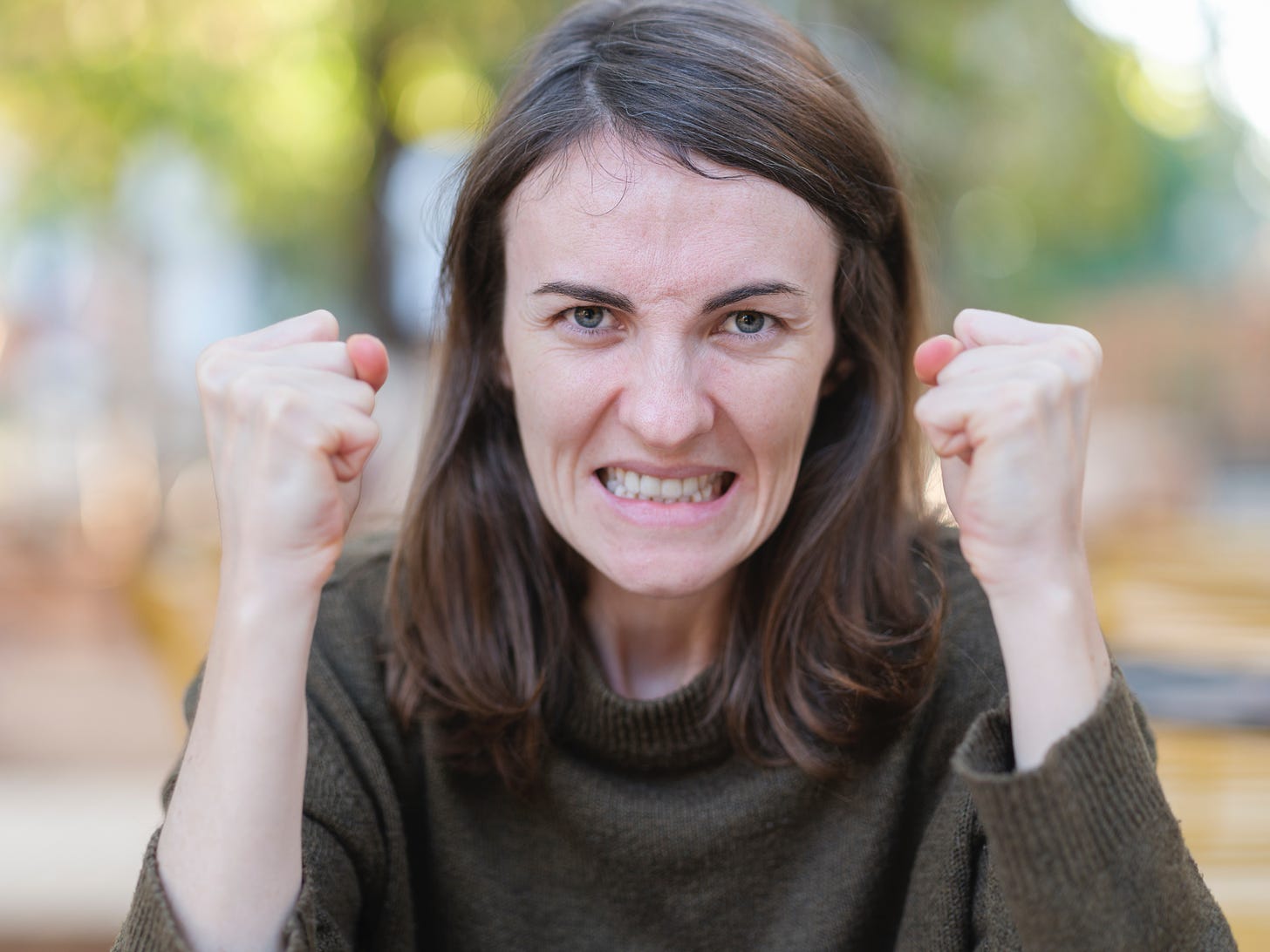 picture of a white woman with brown shoulder length hair making an angry face and holding up both clenched fists.