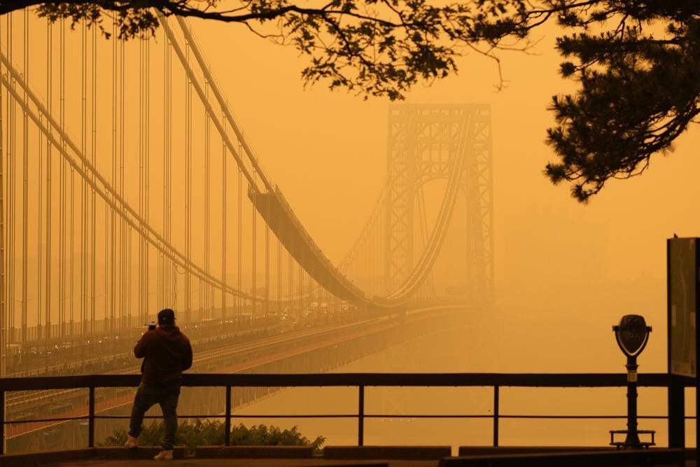 CORRECTS DATELINE TO FORT LEE, NOT ENGLEWOOD CLIFFS - A Man talks on his phone as he looks through the haze at the George Washington Bridge from Fort Lee, N.J., Wednesday, June 7, 2023. Intense Canadian wildfires are blanketing the northeastern U.S. in a dystopian haze, turning the air acrid, the sky yellowish gray and prompting warnings for vulnerable populations to stay inside. (AP Photo/Seth Wenig)