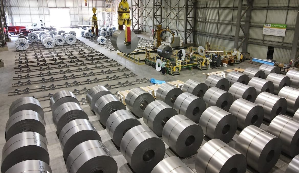 A large warehouse facility filled with rolls of shiny silver metal material wrapped up in coils