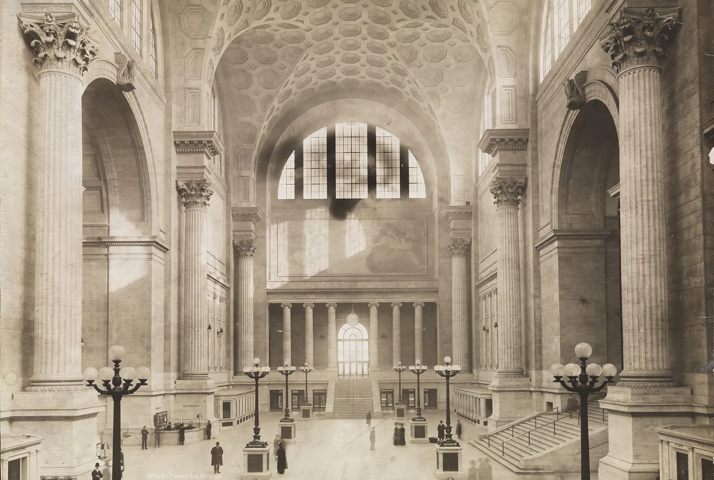 Sepia photo of NYC's Penn Station, with high ceilings & stone columns