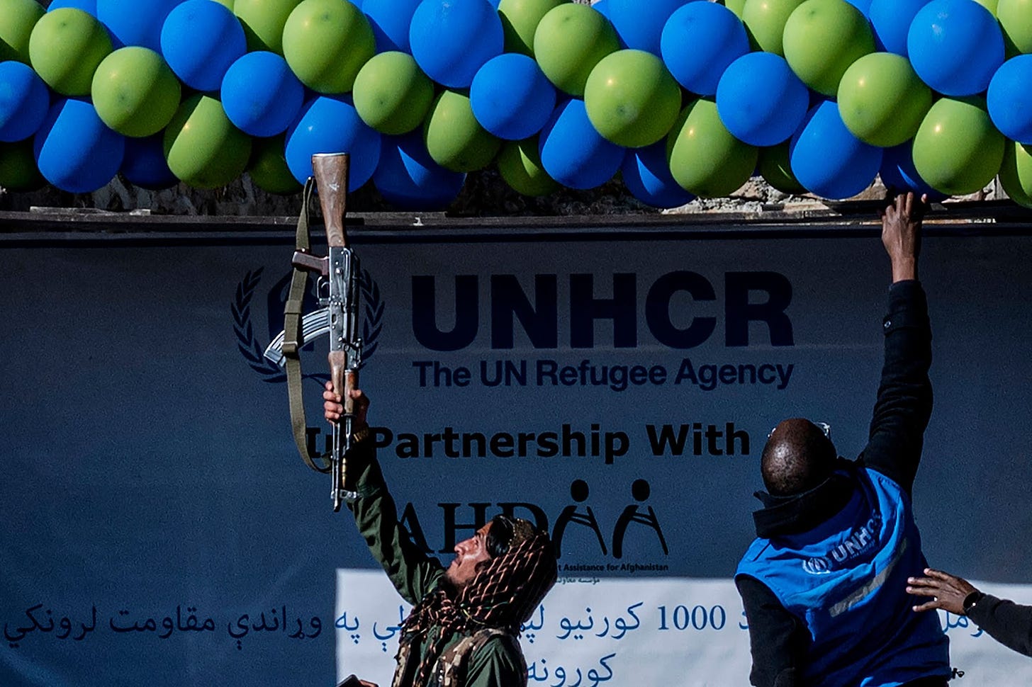 <p>A member of Taliban security adjust balloons with his gun during a handover ceremony of newly built houses constructed by the United Nations refugee agency (UNHCR) in Paktika province</p>