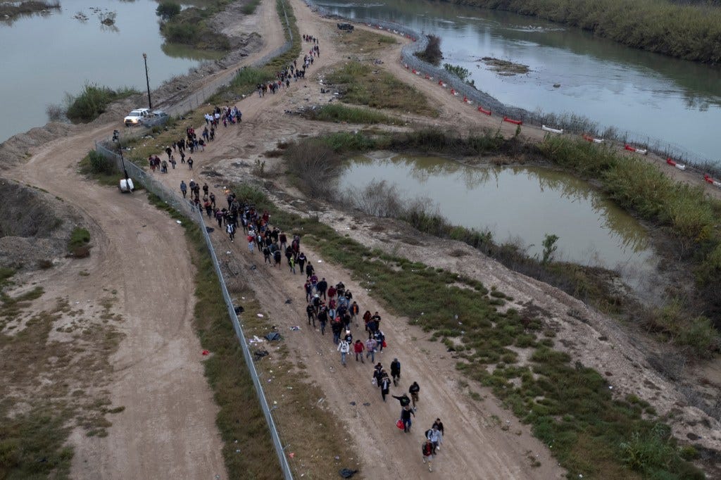 Migrants wade through the Rio Grande River and walk along a dirt road to a processing center in Eagle Pass, Texas.