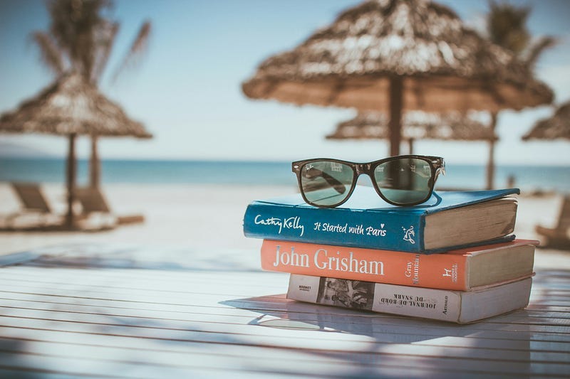 beach scene, with three books, a sunglasses and the view of the sea.