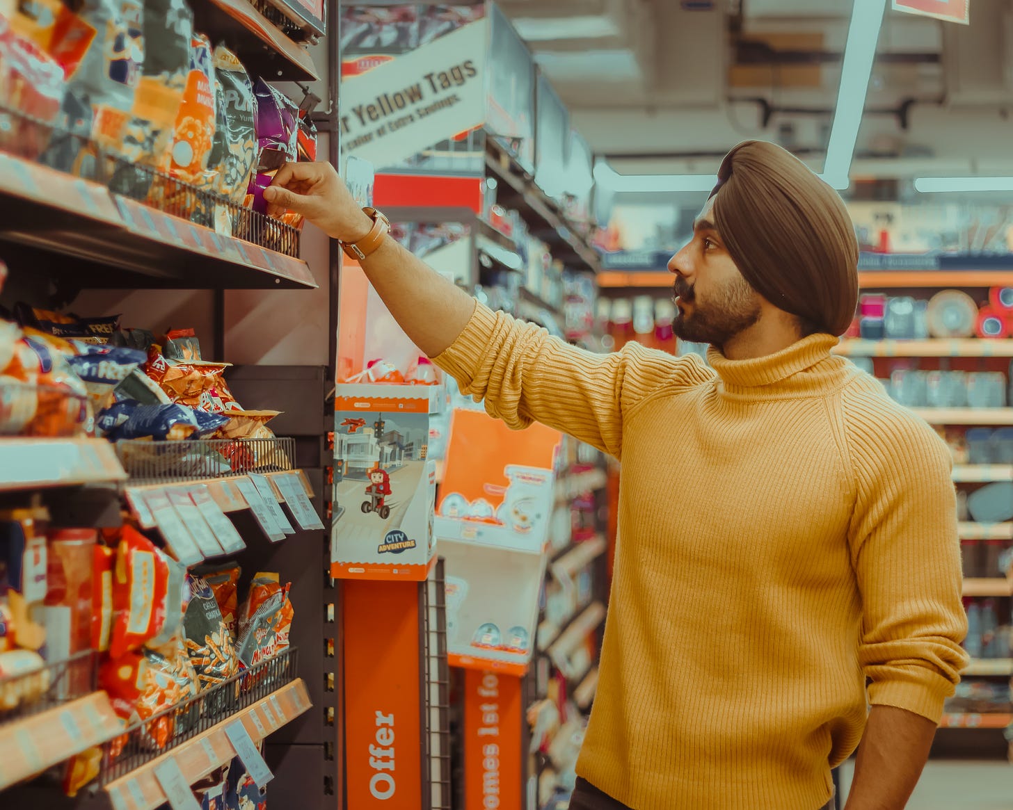 A man wearing a yellow sweater, browsing in a supermarket aisle