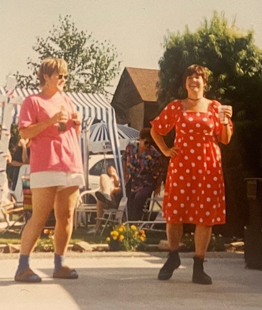 Blond young woman in shorts and brunette yong woman in a red and white polkadotted dress. Holding beers and smiling outside