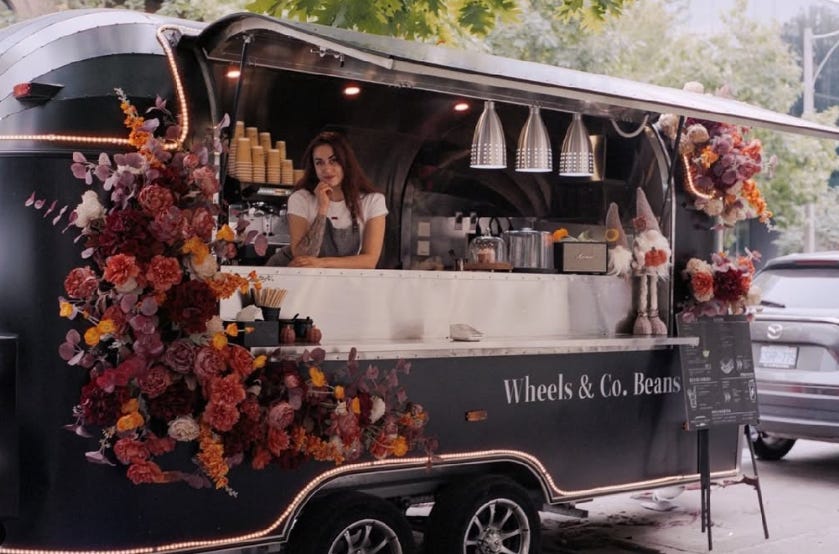 A photo of a black trailer setup to sell coffee and baked goods