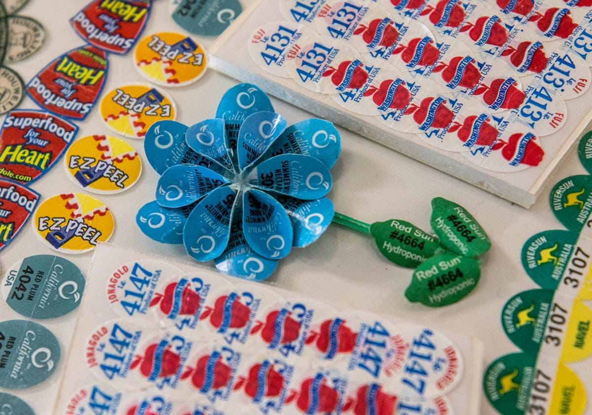 A photograph of a three-dimensional six-petaled flower made from fruit stickers, which is part of a larger fruit sticker collage.